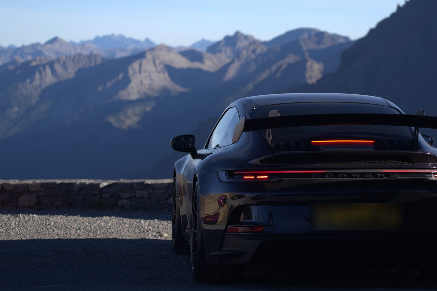 A dark sports car parked above layers of mountain ridges at dusk